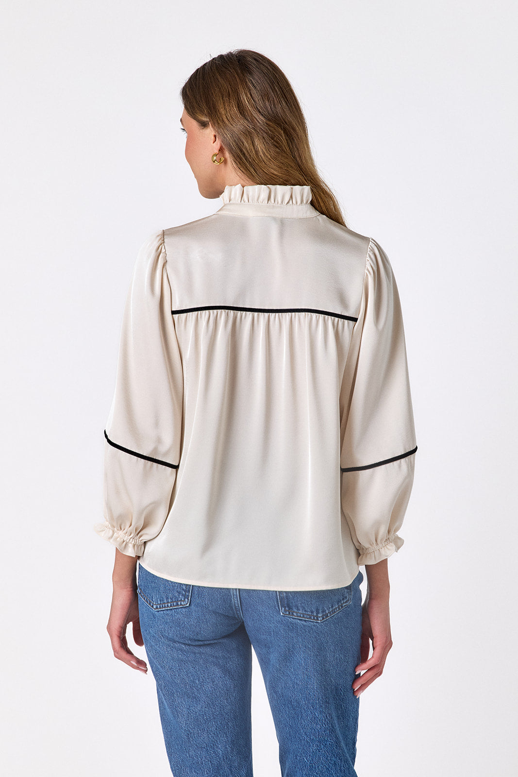 Back view of the Crosby Worth Blouse in ivory showing the gathered back yoke, black contrast piping, ruffled collar, and full sleeves.