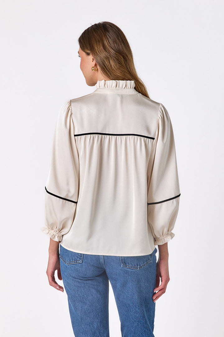 Back view of the Crosby Worth Blouse in ivory showing the gathered back yoke, black contrast piping, ruffled collar, and full sleeves.