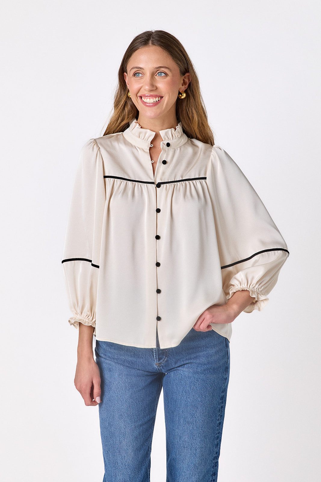 Model wearing the Crosby Worth Blouse in ivory with black contrast piping, black buttons, ruffled collar, and voluminous sleeves.