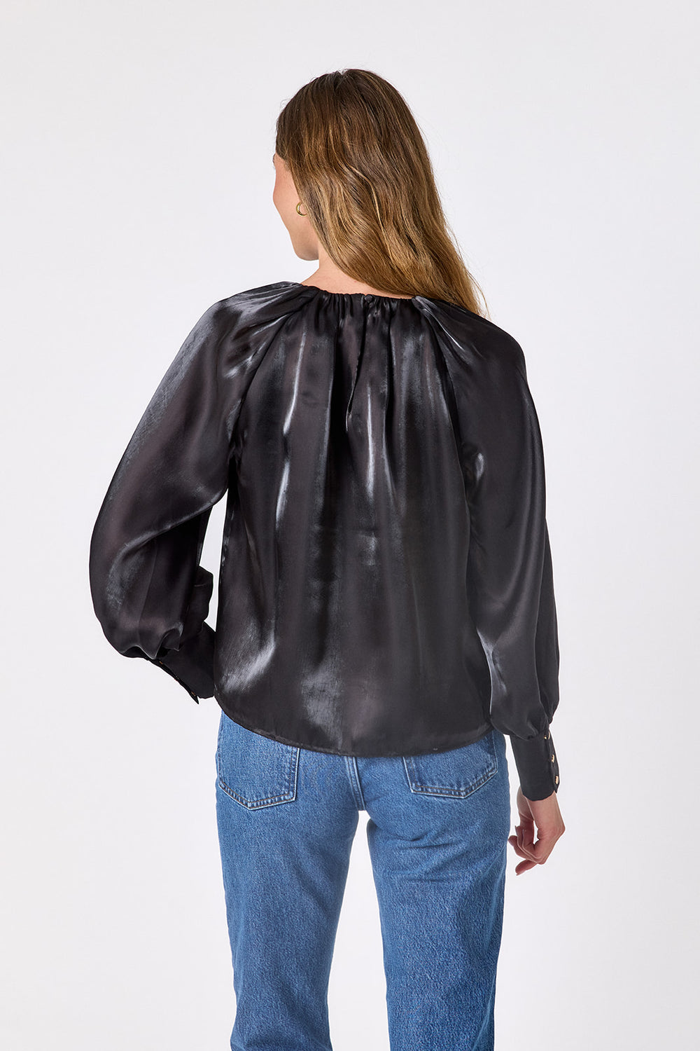 Crosby Elizabeth Blouse in Black, close-up of the lustrous satin fabric, gathered neckline, and deep cuff with three gold buttons
