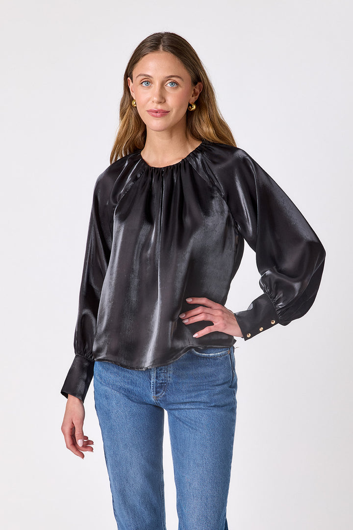 Crosby Elizabeth Blouse in Black, front view on model showing gathered round neckline, raglan balloon sleeves, and gold-buttoned cuffs, worn with light-wash straight-leg jeans
