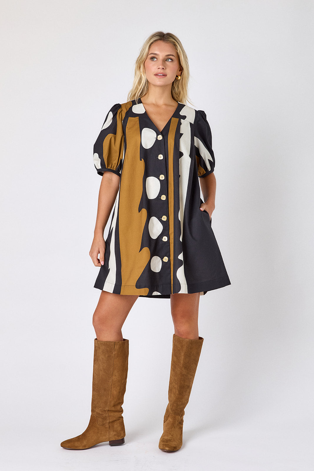 Crosby Stevie Dress in black, camel, and ivory "Wild Line" abstract print, styled with a V-neckline, puff sleeves, and full button front, worn with suede knee-high boots against a white backdrop.