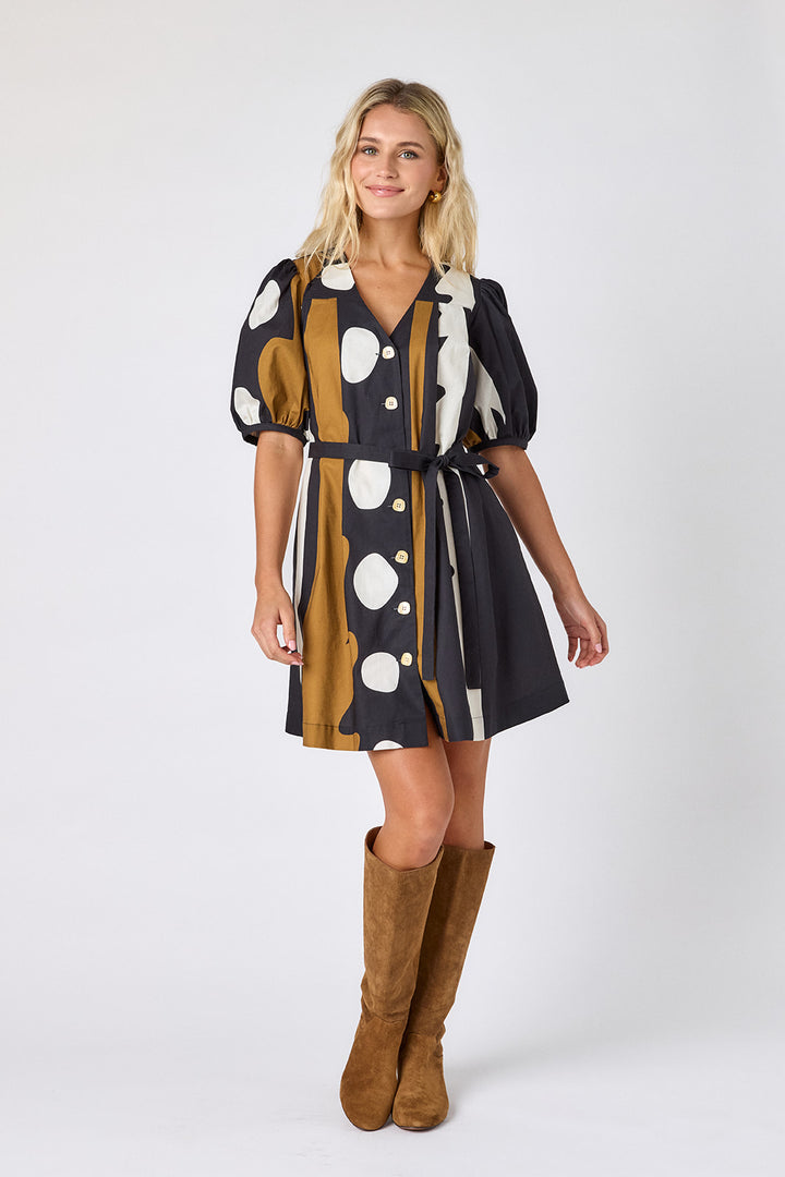 Crosby Stevie Dress in black, camel, and ivory "Wild Line" abstract print, styled with a V-neckline, puff sleeves, and full button front, worn with suede knee-high boots against a white backdrop shown belted.
