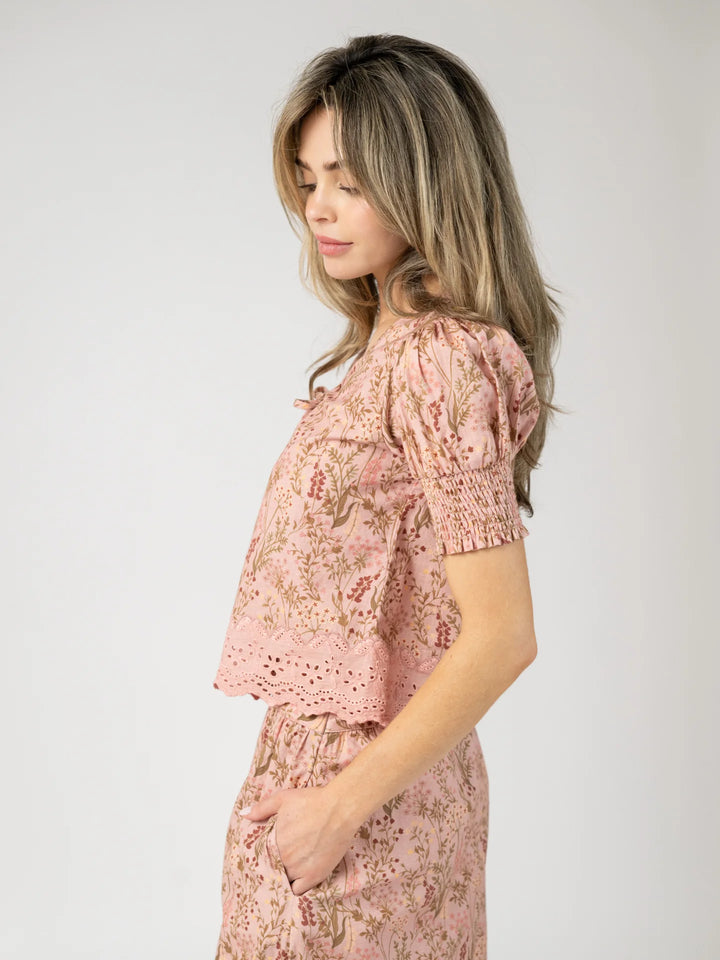 Side profile view of a woman wearing the Louisa Top in Autumn Stems Rose, showing the cropped length, smocked sleeve cuff, and scalloped eyelet lace hem.