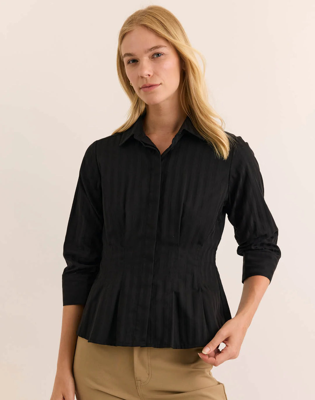 Hinson Wu 3/4 Sleeve Martina Top in solid black with tonal self-stripe, styled with a point collar and fitted, pleated peplum waist, worn with camel trousers against a neutral backdrop.