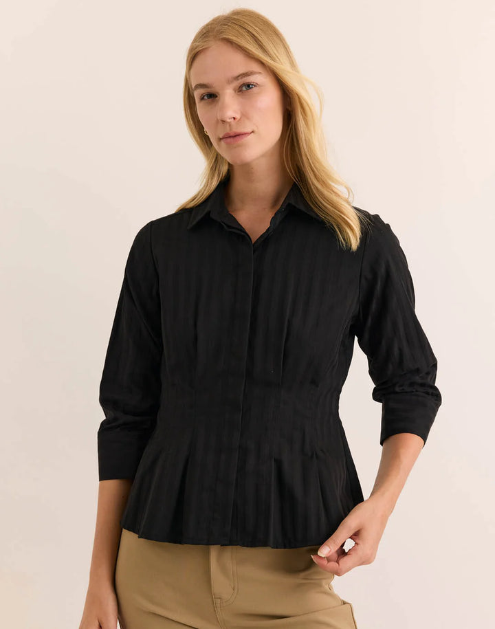 Hinson Wu 3/4 Sleeve Martina Top in solid black with tonal self-stripe, styled with a point collar and fitted, pleated peplum waist, worn with camel trousers against a neutral backdrop.