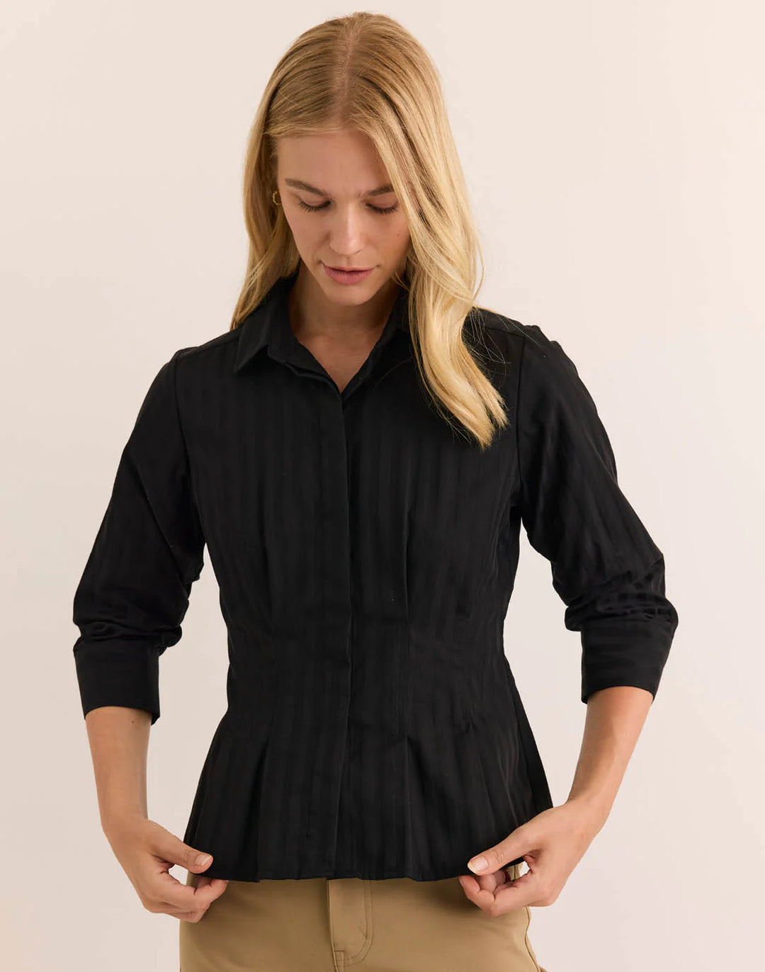 Hinson Wu 3/4 Sleeve Martina Top in solid black with tonal self-stripe, styled with a point collar and fitted, pleated peplum waist, worn with camel trousers against a neutral backdrop. 2