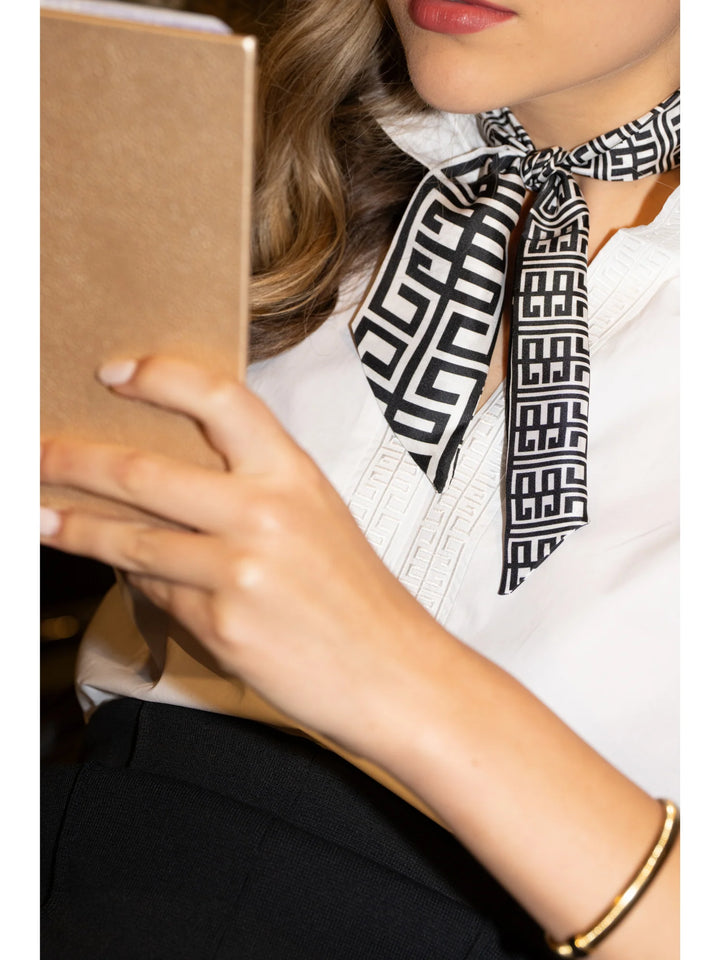 Emily McCarthy Silk Scarfette in Black Greek Key — detail close-up, tied at the neck over a white embroidered top, showing bold-scale Greek key pattern