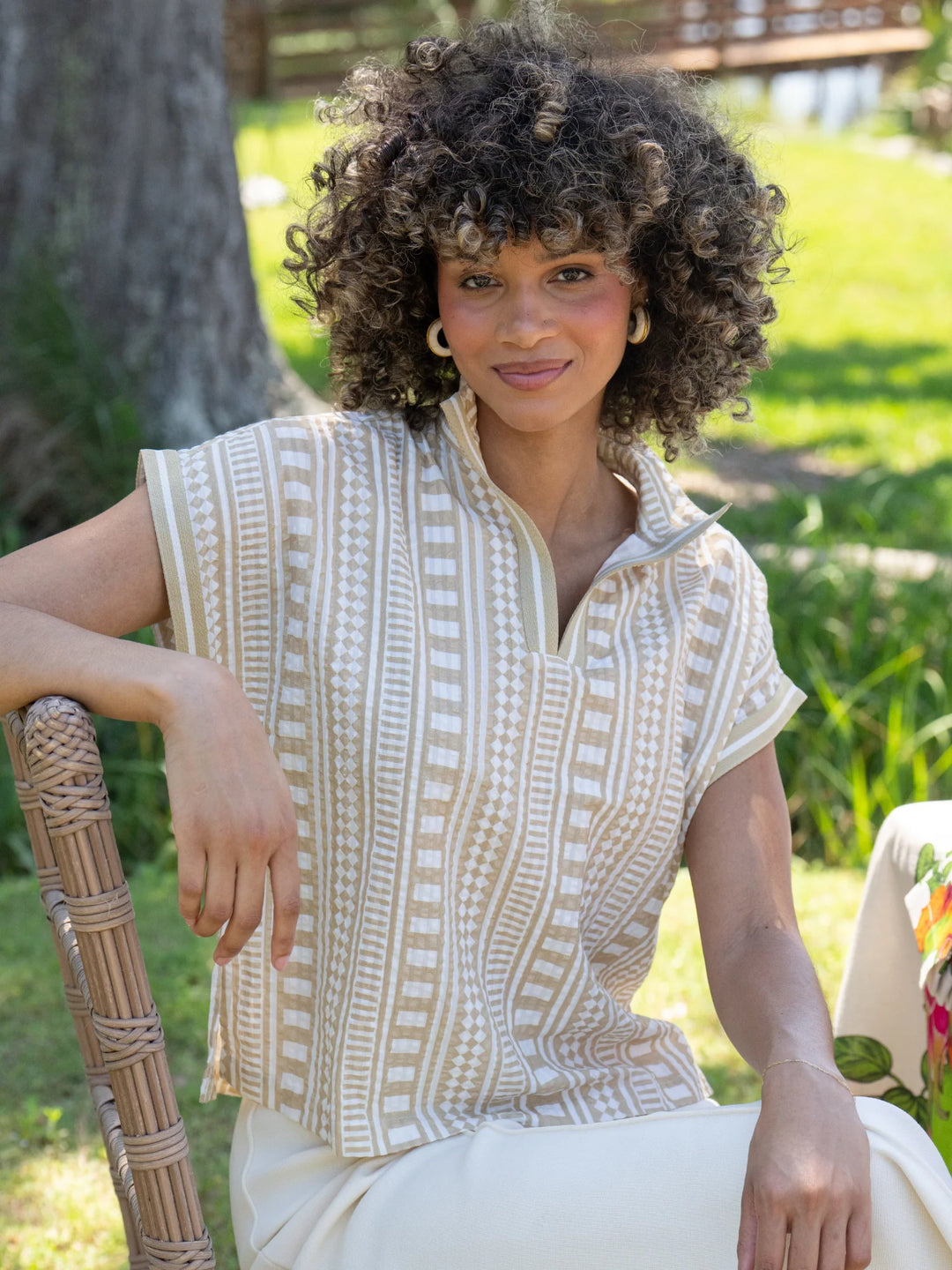Emily McCarthy Riviera Top in Piazza Stripe, sand and white geometric vertical stripe cotton top with stand collar and dolman sleeves on model in garden.
