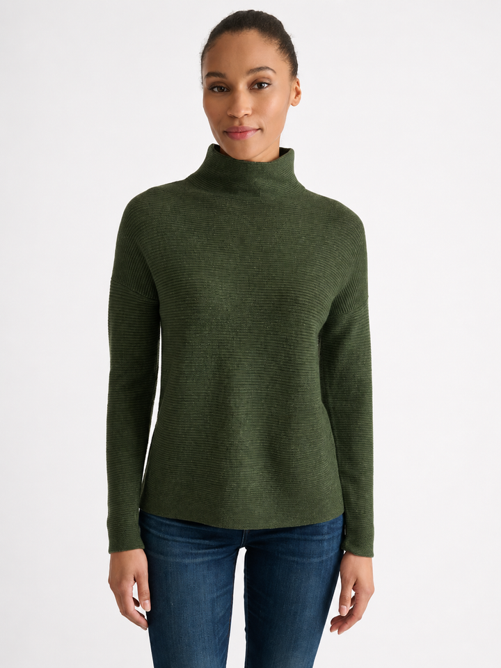 Woman wearing a highland green textured rib cashmere funnel neck sweater with long sleeves, paired with jeans.