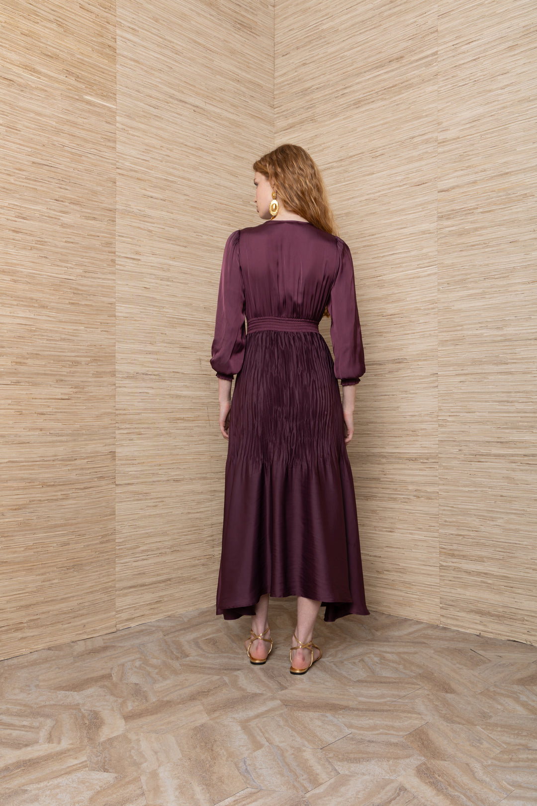 Hale Bob Yamileth V Neck Long Dress in Plum, back view on model, showing smocked waistband, pintuck-pleated skirt, blouson sleeves with smocked cuffs, and uneven midi hem.