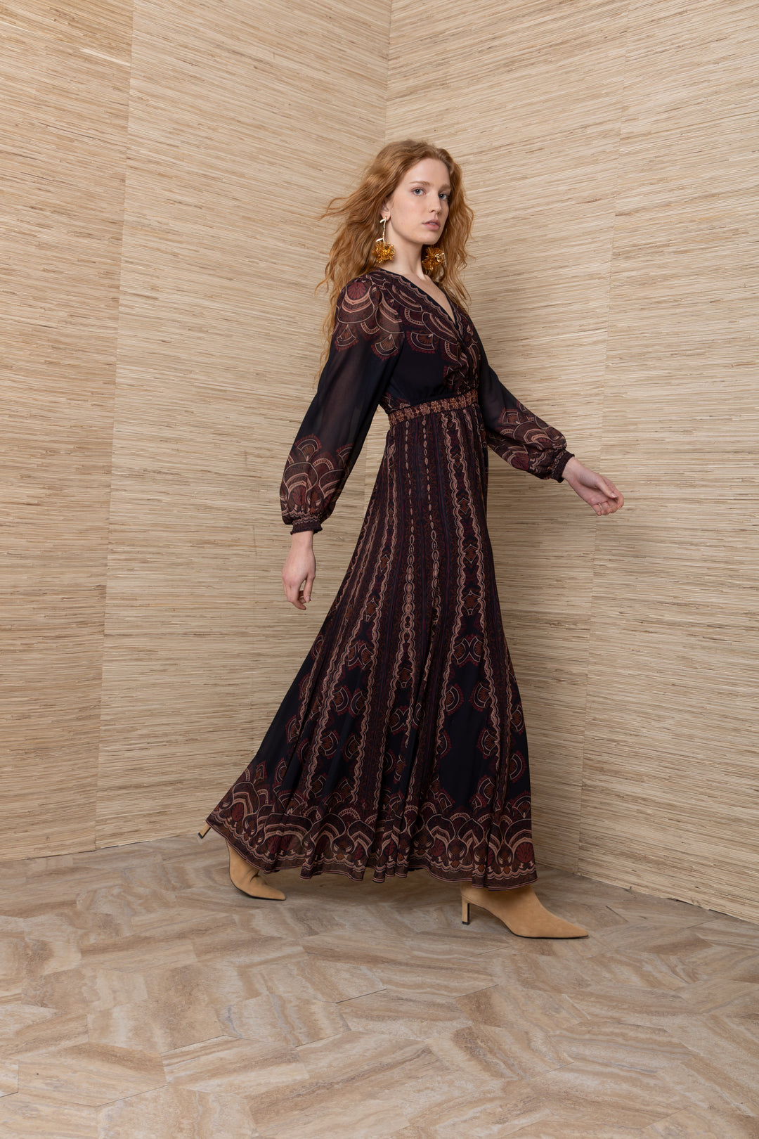 Hale Bob Iselda V Neck Maxi in Plum Multi, side view of model walking, showing sheer printed sleeves, smocked waist, and full maxi skirt in motion.