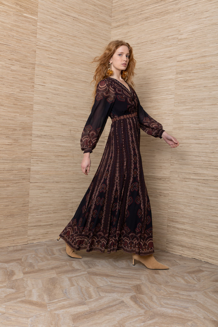 Hale Bob Iselda V Neck Maxi in Plum Multi, side view of model walking, showing sheer printed sleeves, smocked waist, and full maxi skirt in motion.
