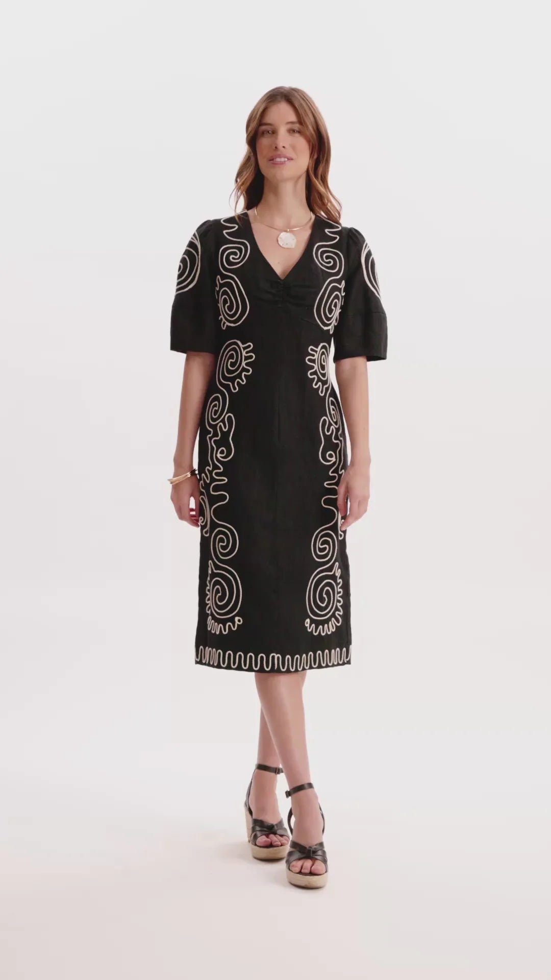 Model wearing Tyler Boe Posey Linen Embroidered Midi Dress in black with cream spiral cord embroidery, styled with black espadrille wedge sandals and gold necklace, full-length front view on white background.