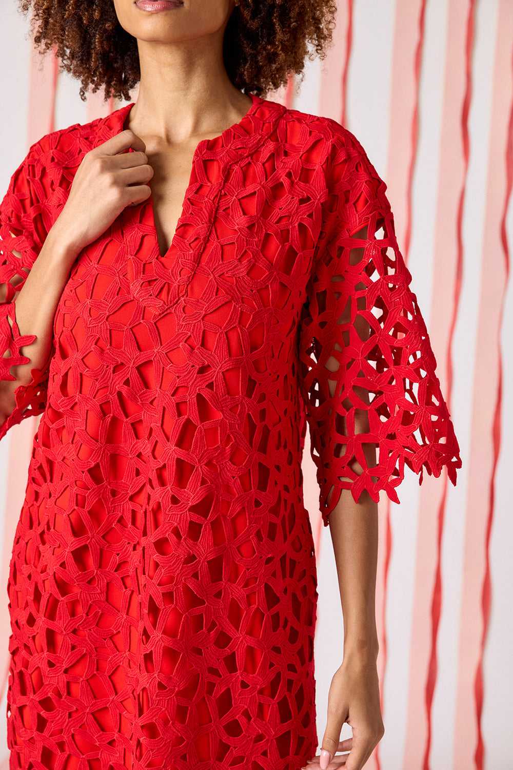 Model wearing Crosby Alice Lace Tunic Dress in Pomegranate styled with gold flat sandals. Dress features all-over geometric crochet lace, V-notch neckline, three-quarter bell sleeves with scalloped hem, and relaxed boxy tunic silhouette.