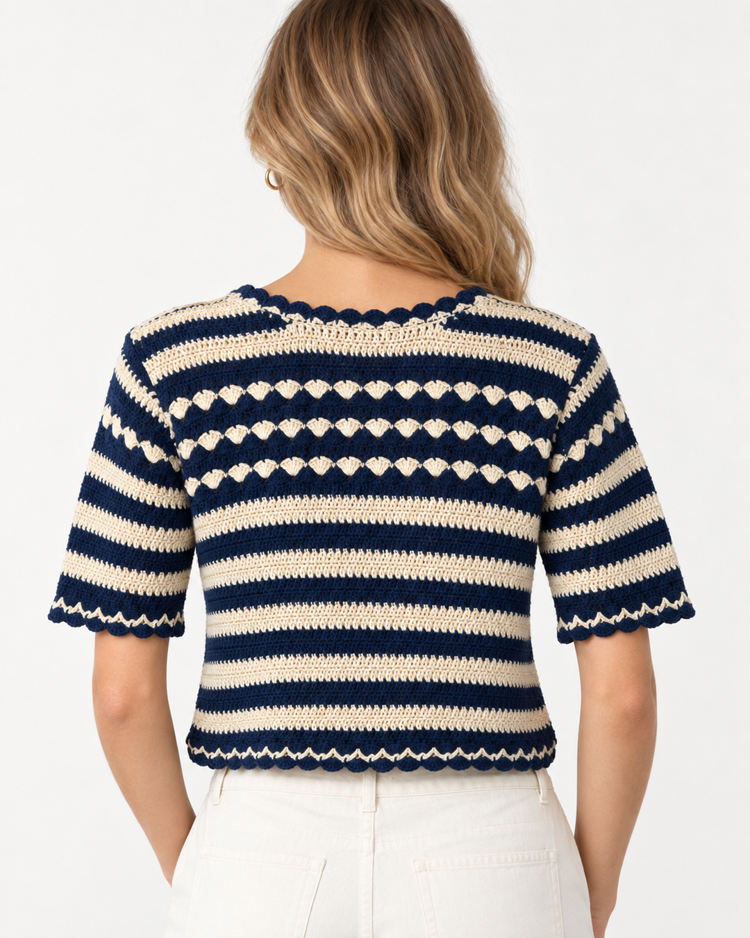 Back view of a model wearing the navy and cream striped crochet sweater with cream trousers, showing the scalloped hem and short sleeves.