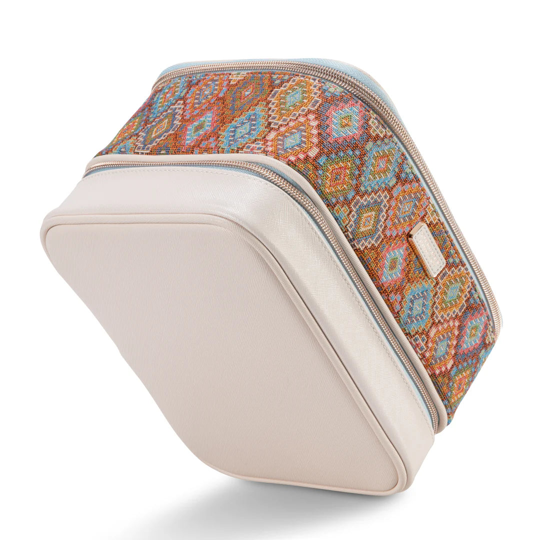 Three-quarter view with badge: Stephanie Johnson Jenny Train Case in Bodrum Kilim print, angled to show two-tier zippered construction, rolled leather handle, and recycled materials badge in upper left corner.