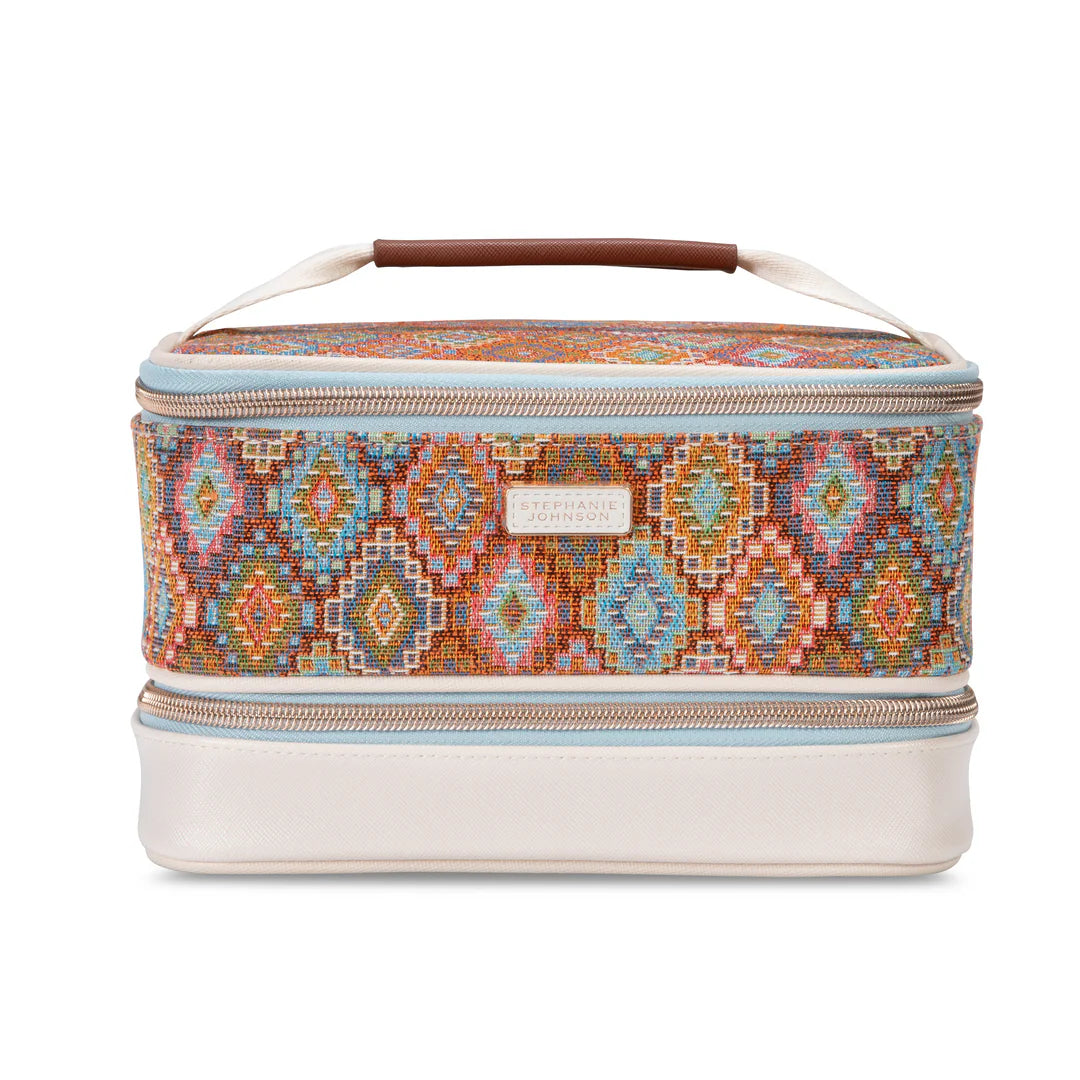 Front full view:  Stephanie Johnson Jenny Train Case in Bodrum Kilim print, showing woven diamond-pattern exterior in rust, blue, and coral tones, ivory faux-leather base trim, and rolled brown leather top handle.  