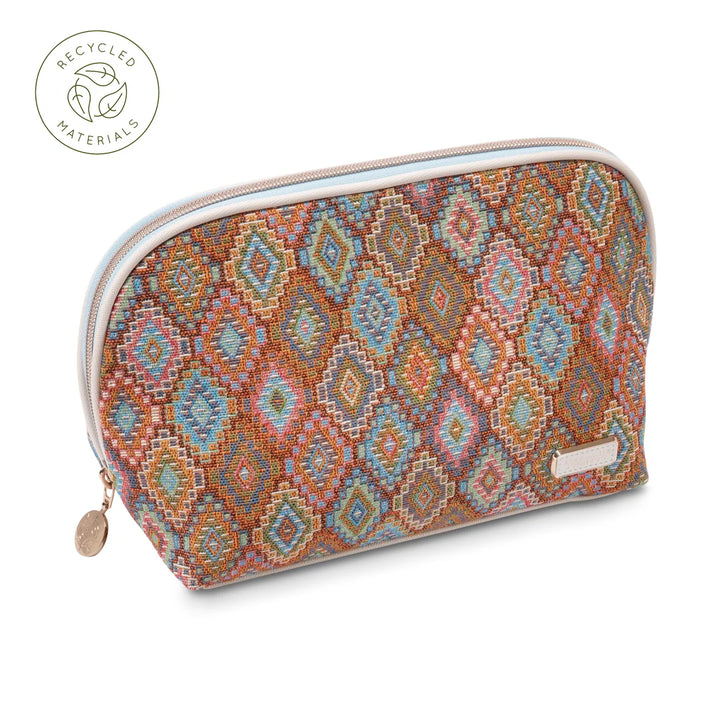 Front view: Stephanie Johnson Lola Makeup Bag in Bodrum Kilim print, showing dome-shaped silhouette with woven diamond-pattern exterior in rust, blue, and coral tones, ivory trim, and rose gold zipper pull with engraved medallion. Recycled materials badge in upper left corner.