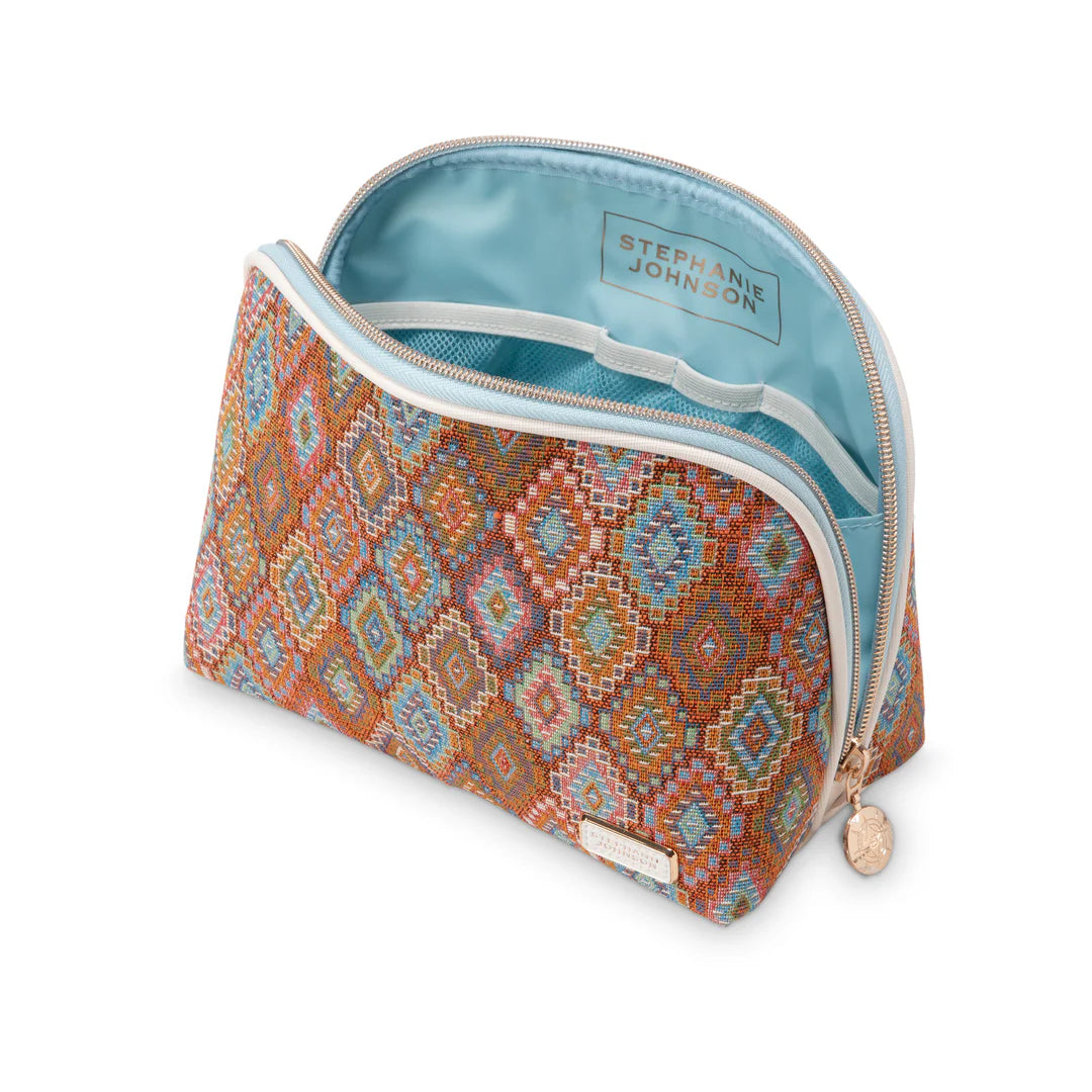 Open/styled view: Stephanie Johnson Lola Makeup Bag open, showing pale blue interior lining and elastic stash pockets, with makeup brush and compact styled alongside.