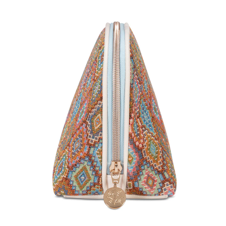 Side/end view 2: Stephanie Johnson Lola Makeup Bag in Bodrum Kilim print, showing triangular end profile, center zipper with ivory trim, and rose gold zipper pull with engraved medallion.