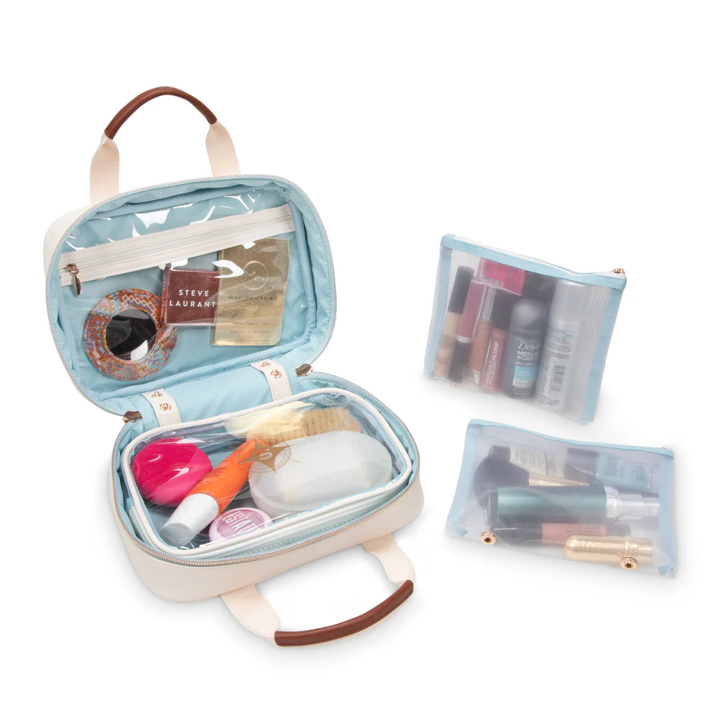 Open/styled view: Stephanie Johnson ML Traveler open and filled with skincare and makeup products, showing pale blue interior lining, clear zip pocket in lid, round mirror compact in coordinating kilim print, and two clear zip pouches packed with cosmetics beside the case.