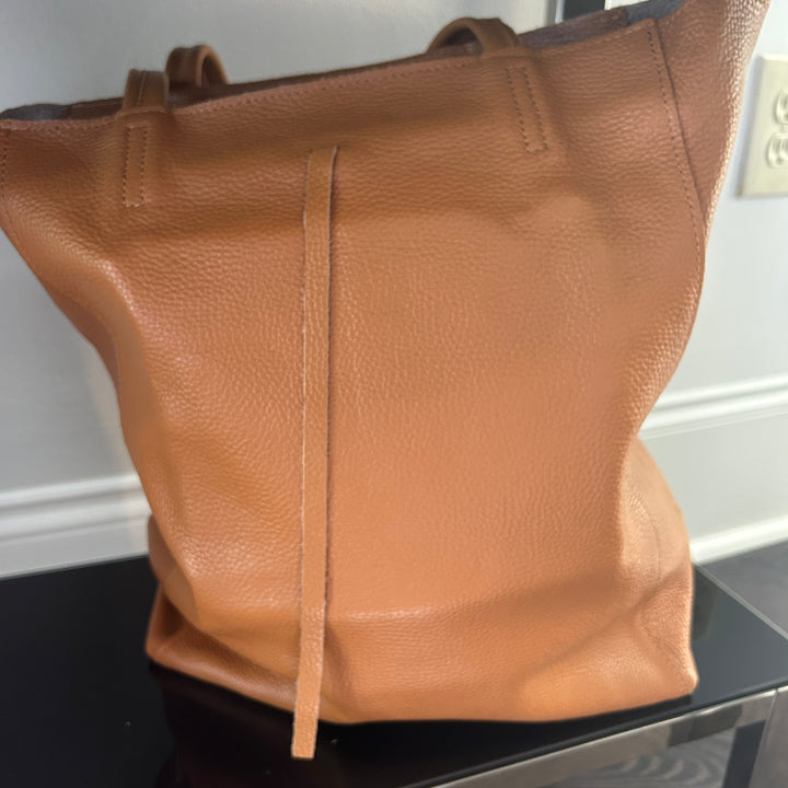 Brown leather handbag on a black surface with a white wall background