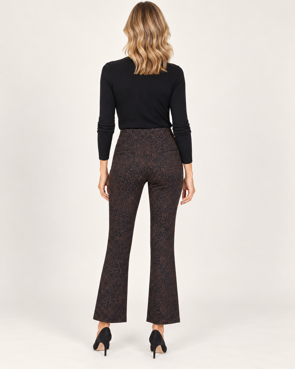 Back view of a model wearing the Elliott Lauren Cool Cat Baby Boot Pant in a chocolate leopard print, paired with a black long-sleeve top and black pumps.
