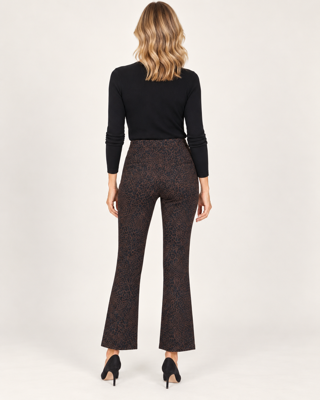 Back view of a model wearing the Elliott Lauren Cool Cat Baby Boot Pant in a chocolate leopard print, paired with a black long-sleeve top and black pumps.
