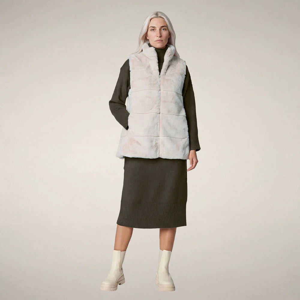 Front view of a woman wearing the Nives Faux Fur Reversible Vest in shore beige over an olive knit sweater dress and cream boots.