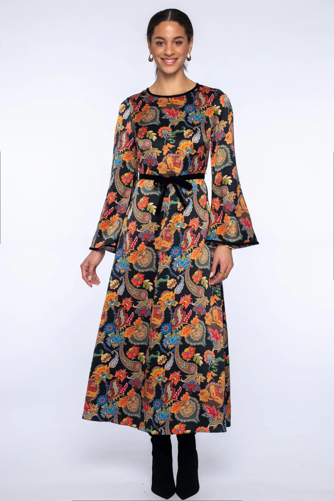 Model wearing the Elizabeth James Lily Long Dress in paisley, featuring long bell sleeves, a maxi-length silhouette, velvet trim, and a black waist tie.