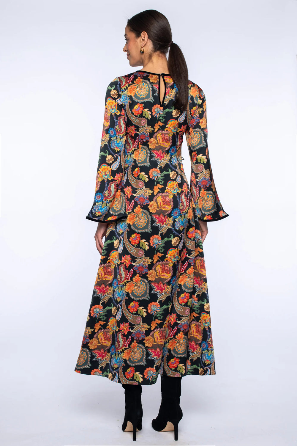 Back view of the Elizabeth James Lily Long Dress in paisley showing the long silhouette, bell sleeves, velvet trim, and back button closure.