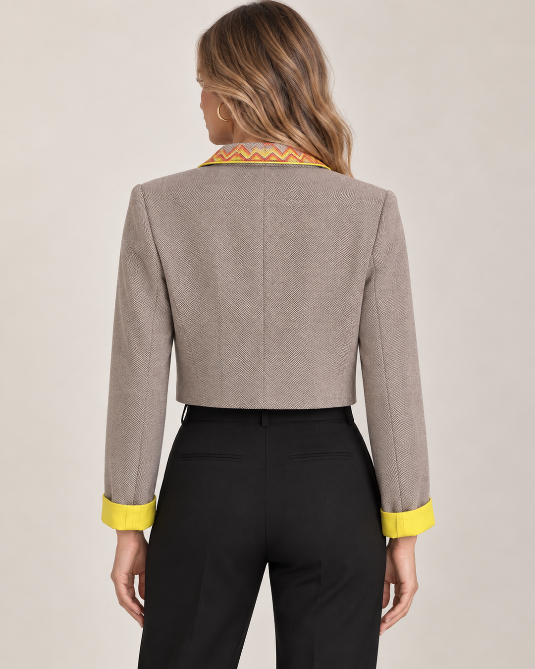 Back view of a model wearing the Eleanor Jacket over a black tank and black trousers, showing the cropped hem and yellow cuff detail.