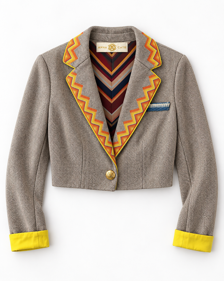 Flat lay of the Anna Cate Eleanor Jacket in taupe herringbone tweed, cropped silhouette, with a chevron-striped orange and yellow trim along the lapel, bright yellow cuffs, and a gold button closure.