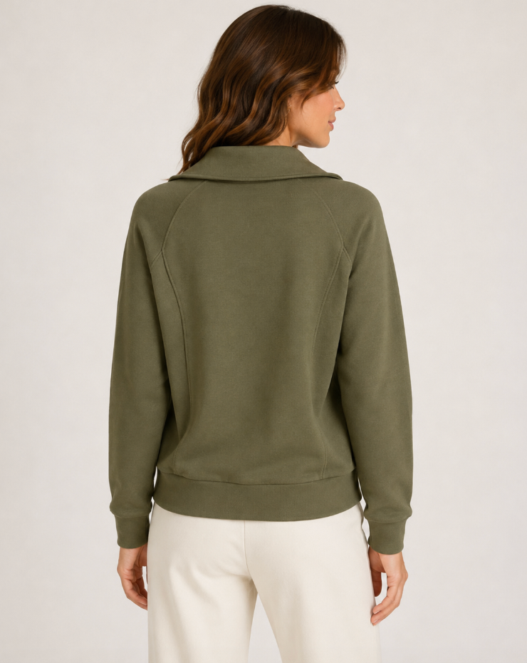 A woman shown from the back wearing an olive green long-sleeve top with a mock neck and white pants, photographed against a plain light gray studio background.