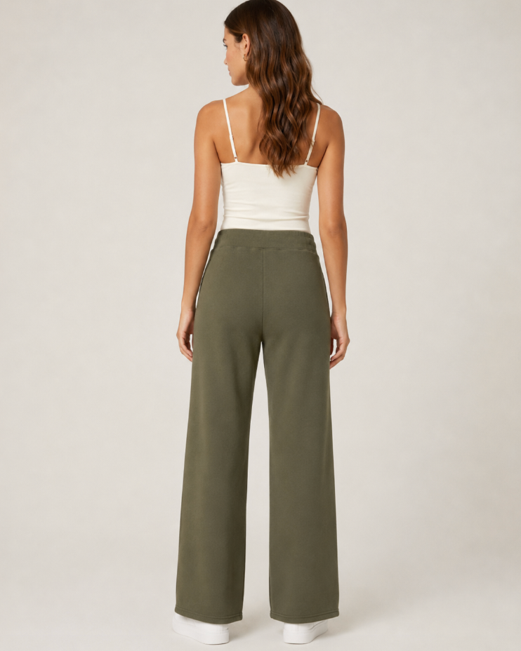 A woman shown from the back wearing olive green wide-leg pants and a white spaghetti-strap camisole top, standing against a plain light gray studio background.