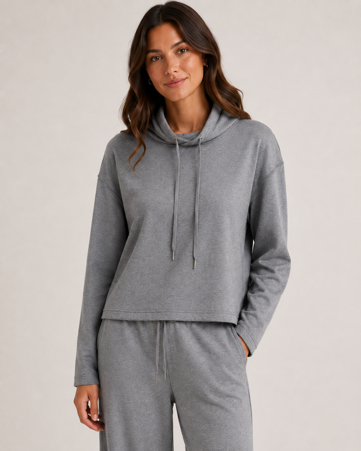 A woman wearing a heather gray cropped hoodie and matching sweatpants, photographed against a plain light gray studio background.
