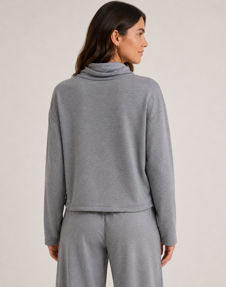 A woman shown from the back wearing a heather gray long-sleeve cowl-neck top and matching gray pants against a plain light beige studio background.