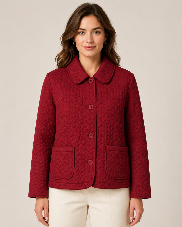 A woman wearing a textured, quilted burgundy cropped jacket with a collar and front buttons, paired with cream pants, against a solid light beige background.