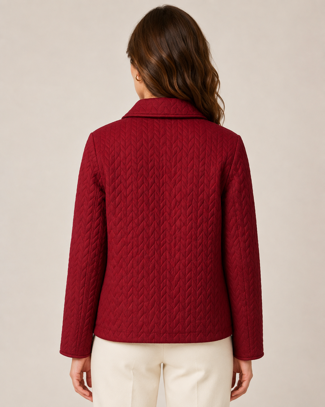 A woman viewed from the back wearing a deep burgundy quilted jacket with cream pants, set against a plain beige studio background.
