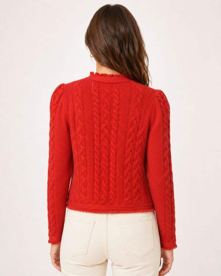 A woman viewed from the back wearing a bright red cable-knit cropped sweater with puffed shoulders and cream-colored pants, set against a plain white studio background.