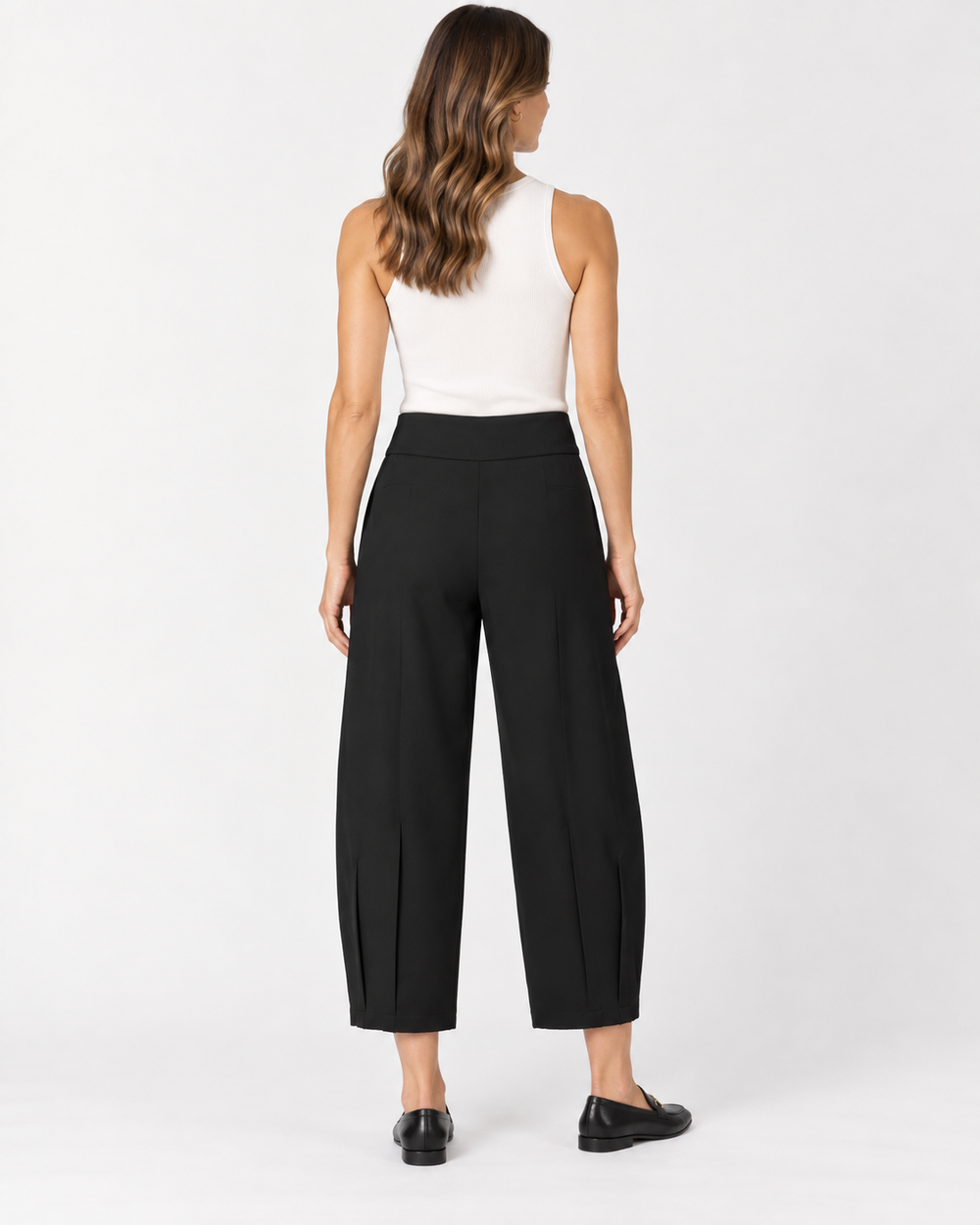 Back view of a woman with long wavy brown hair wearing a white ribbed tank top and Elliott Lauren black barrel-leg cropped pants with side hem vents, paired with black loafers, against a light gray background.