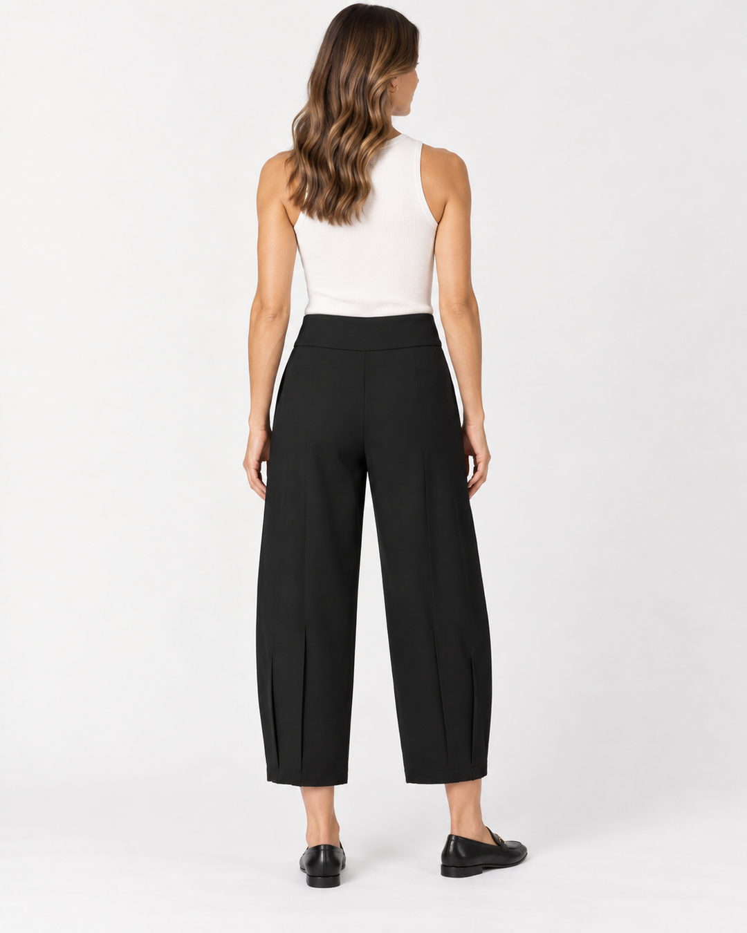 Back view of a woman with long wavy brown hair wearing a white ribbed tank top and Elliott Lauren black barrel-leg cropped pants with side hem vents, paired with black loafers, against a light gray background.