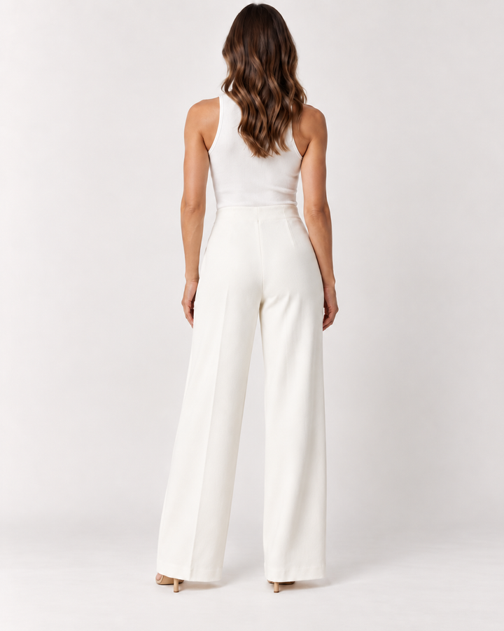 Back view of a woman with long wavy brown hair wearing a white ribbed tank top and Elliott Lauren wide-leg ponte pants in winter white, paired with nude open-toe heels, against a light gray background.