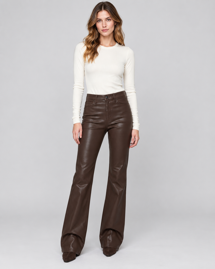 Pistola Evie High Rise Slim Boot in Coated Mocha, front view on model from the shoulders down, showing high rise, glossy chocolate brown coated finish, slim thigh, and boot flare over brown suede boots, paired with a cream ribbed top.