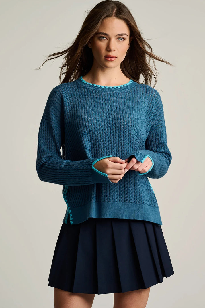 Woman wearing a blue sweater and black pleated skirt on a plain background