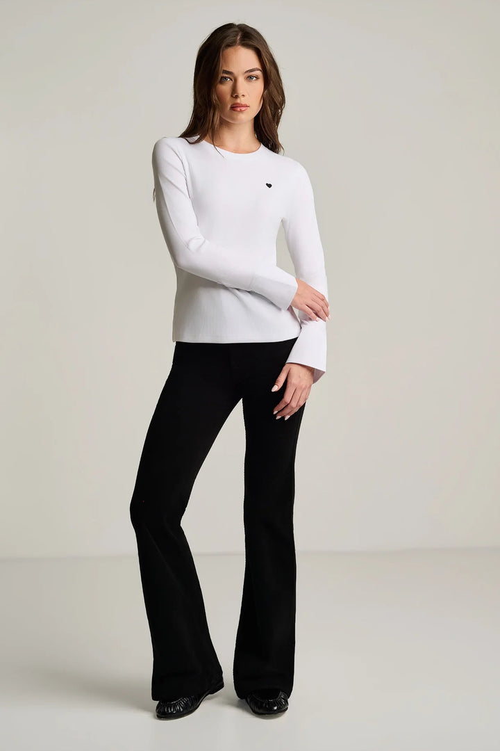 Full-length front view of a woman wearing the Pure Rib Cuff Top in white, tucked into black flared pants with black shoes.