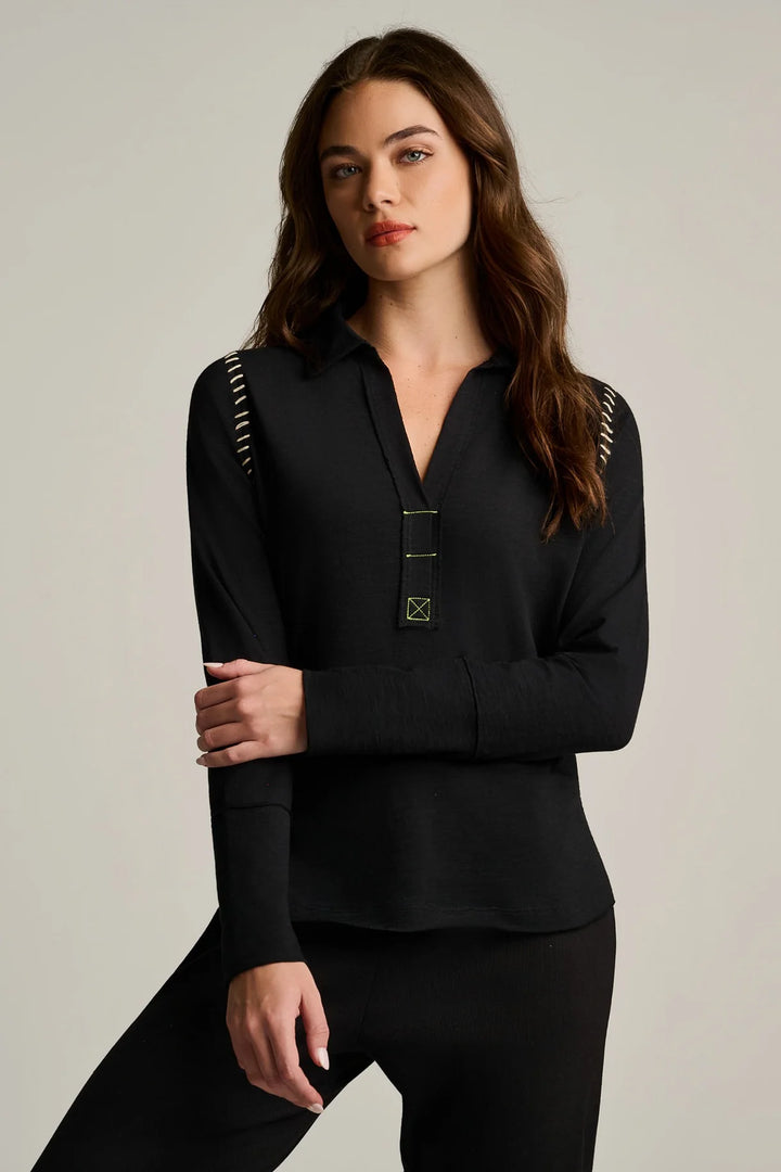 Woman wearing a black long-sleeve top with decorative elements on a neutral background
