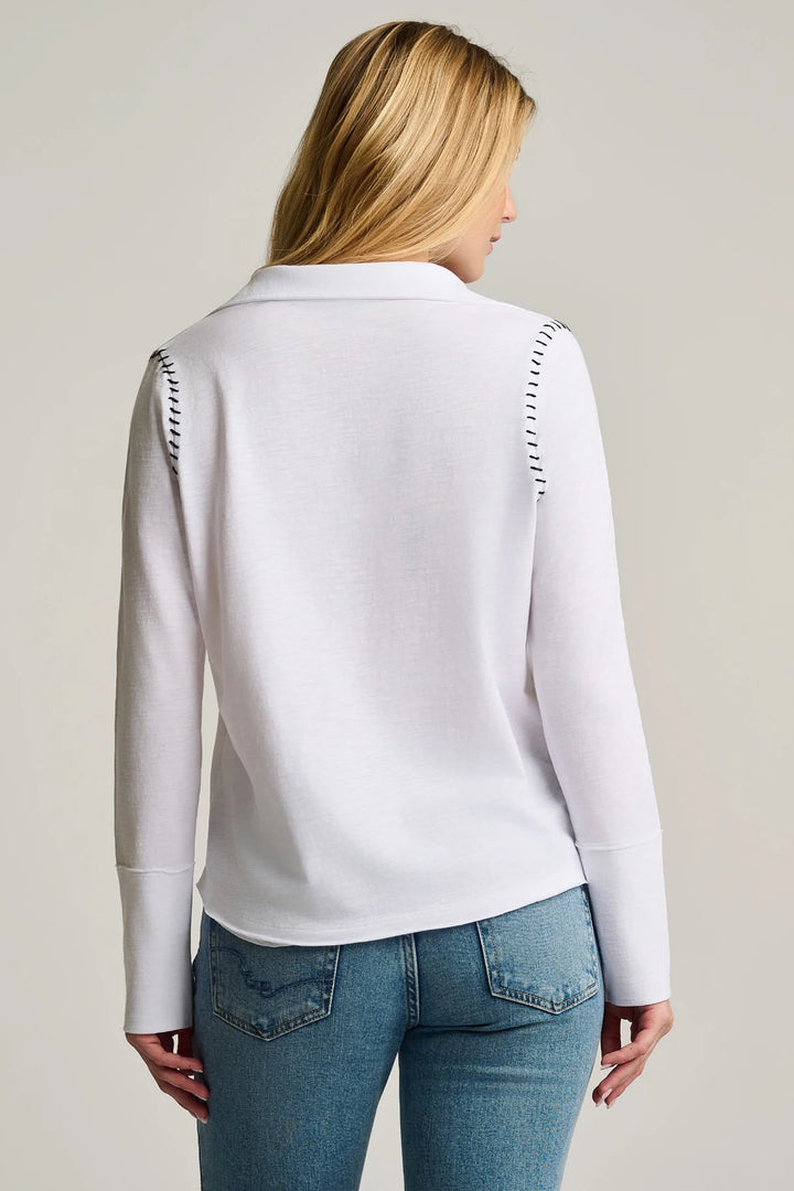 Person wearing a white long-sleeve top with decorative stitching on a plain background
