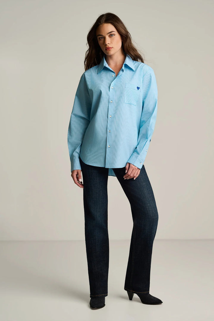 Woman wearing a light blue shirt and dark jeans against a plain background